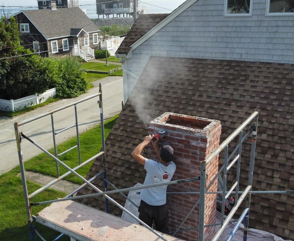 Chimney mason repairing a brick chimney on residential rooftop scaffolding in Massachusetts